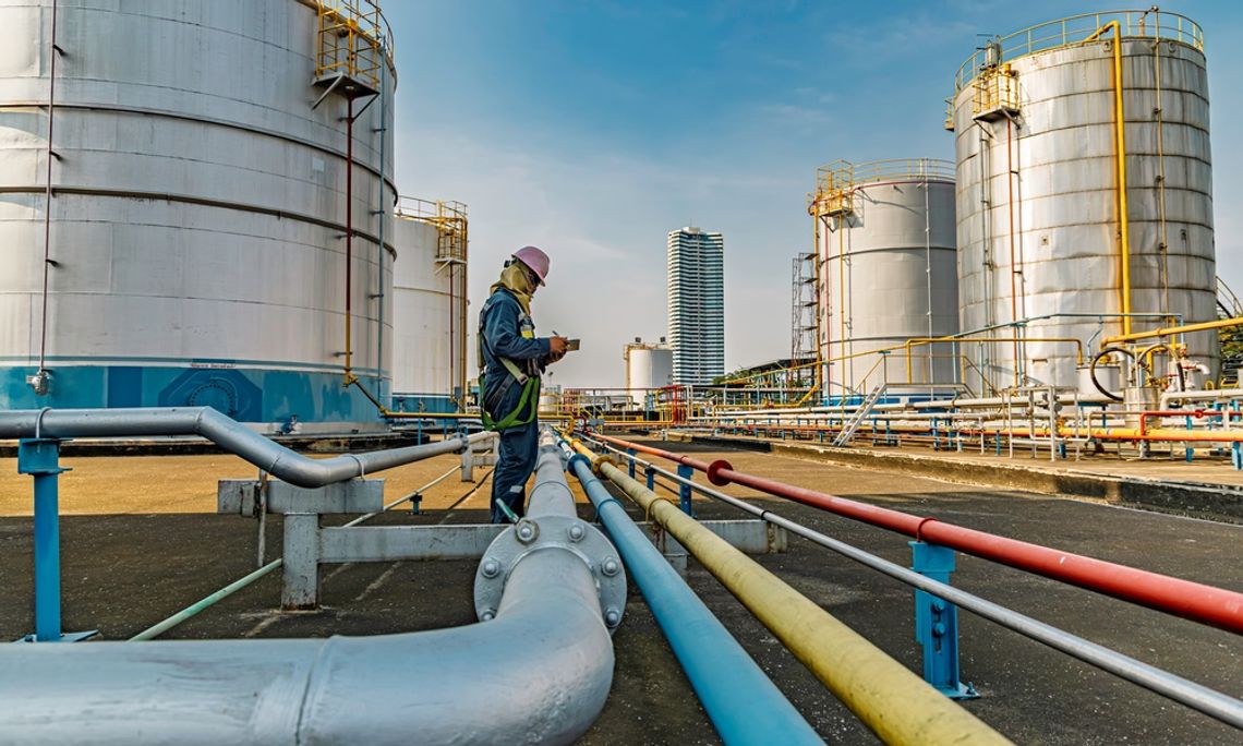When to Repair, Retrofit, or Replace an Industrial Tank a worker in safety gear using a tablet among colorful pipelines and large storage tanks at an industrial site.