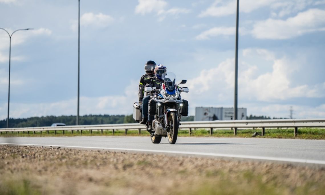 Why a Cruiser Motorcycle Is the Lifestyle Upgrade You Need A motorcycle with a small windshield carrying the rider and a passenger in the back down a sunny concrete road.