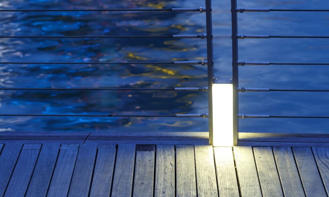 A wooden deck looks out over a body of water. Metal railing held together by cable runs along the deck.