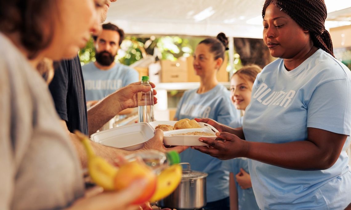 An outdoor food drive event where volunteers of diverse ethnicities serve individuals free food and water.