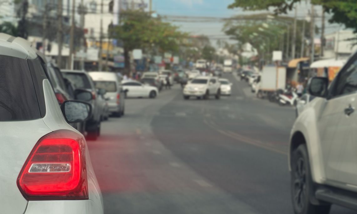 A close-up of the taillight of a white vehicle with its brakes on. A line of cars in a city is blurred ahead of the vehicle.