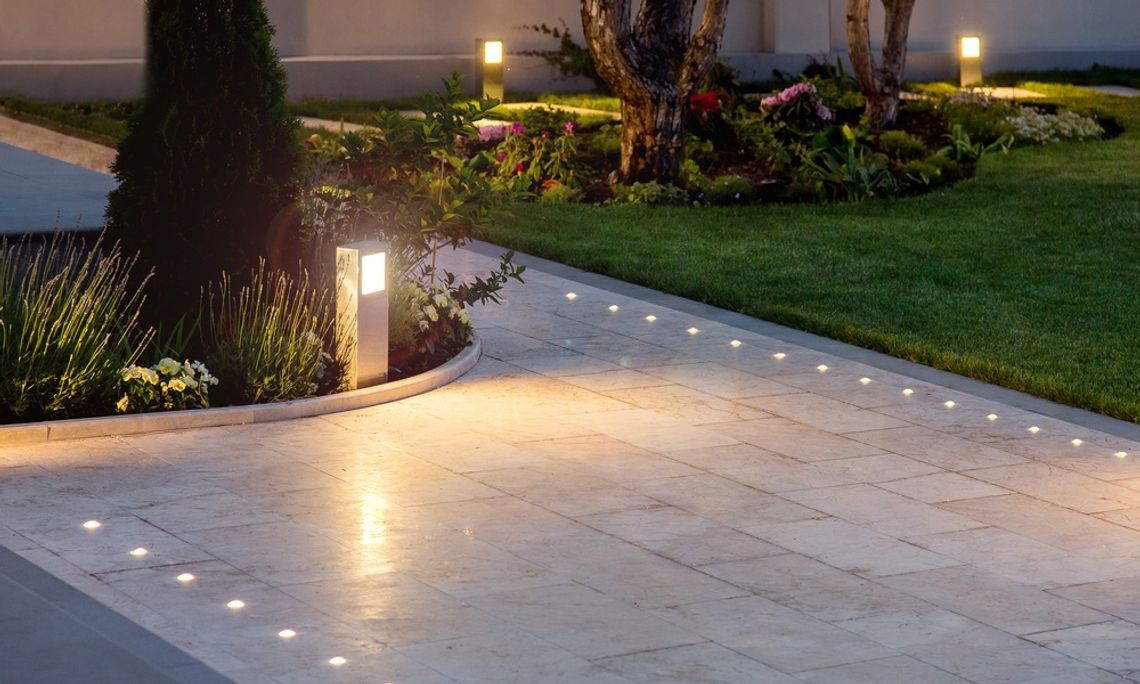 A residential walkway is illuminated by small, circular lights that are in the pavers. Other lighting appears in the landscaping.