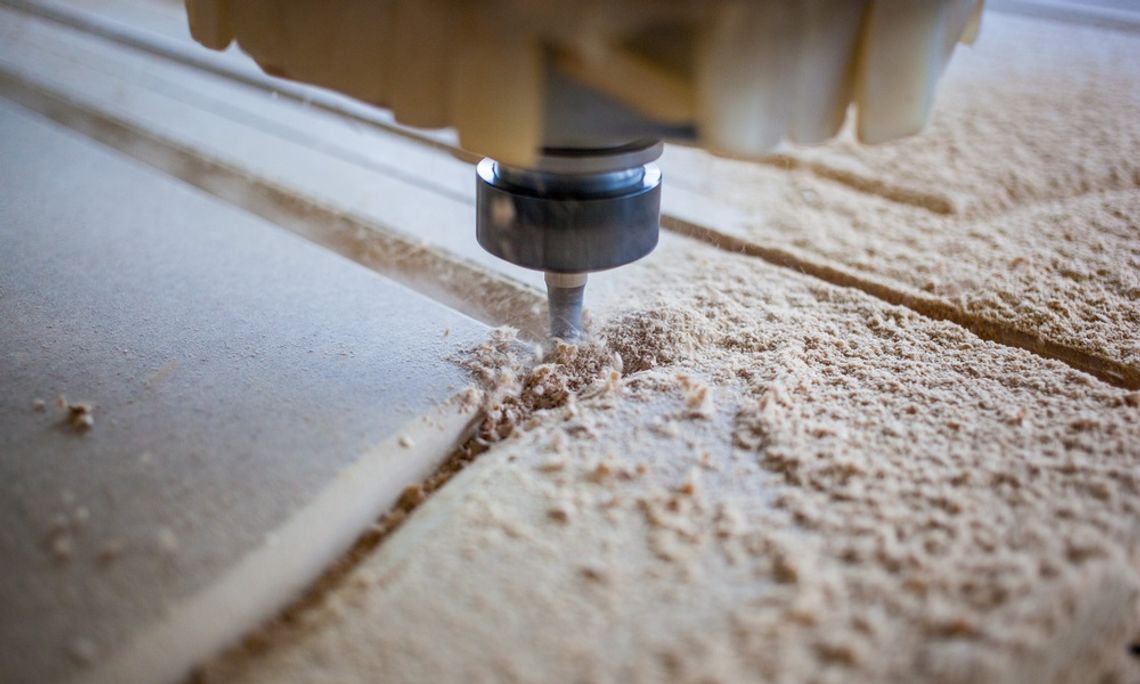 A CNC machine carves precise grooves into wood, scattering fine shavings during an active milling process.
