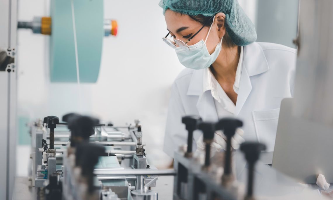 A professional woman doctor is wearing protective gear and glasses while working in a manufacturing setting.