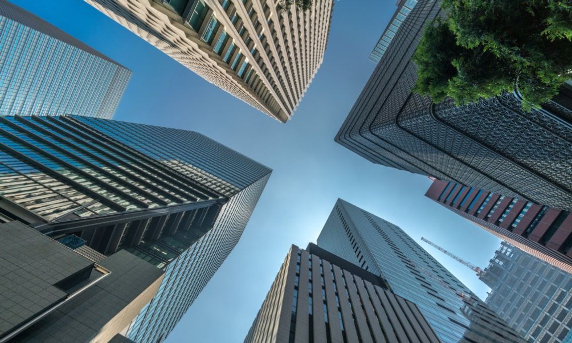 A ground-view looking up at several very tall buildings with multiple stories. The sky is clear and blue.
