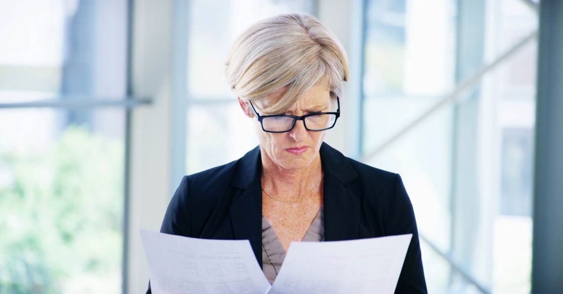 Why the Cheapest Business Quote Can Cost You More A businesswoman wearing glasses compares two printed documents while standing in a bright modern office.
