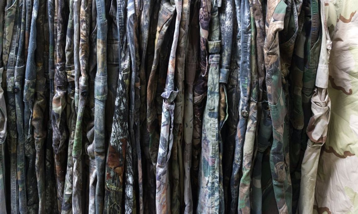 A rack full of camouflage pants in a store. All the pants have camo patterns, but some are lighter colors than others.